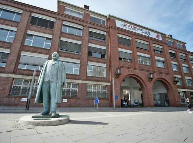 Location Rüsselsheim. Entrance to Motorworld Rüsselsheim. Red brick building with a statue in front of it.