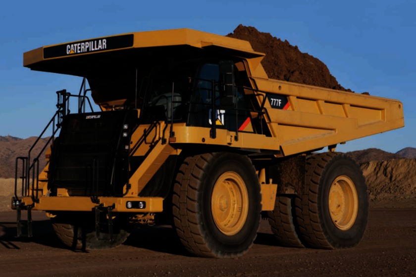 A yellow Caterpillar Mining heavy-duty dump truck filled with earth under a blue sky.