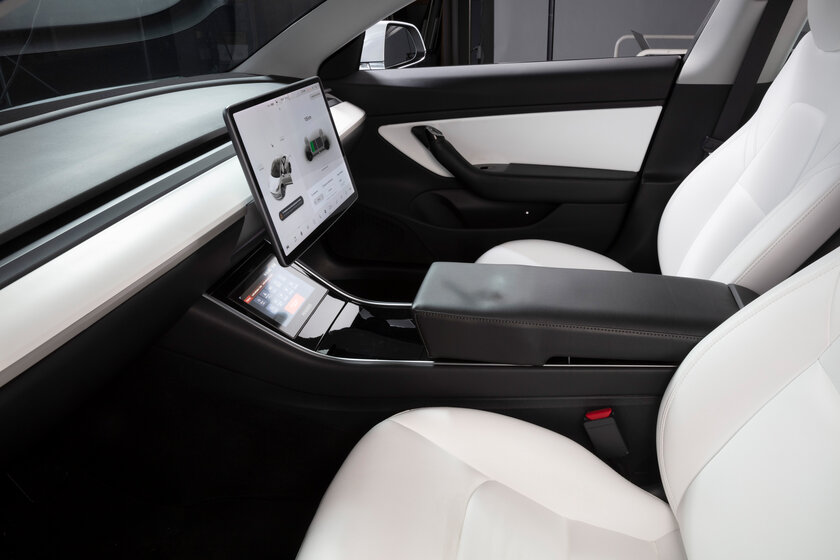 From the window next to the driver's seat, you can see the elegant black and white cockpit of a car, without a steering wheel, only with a touch display in the middle of the car.