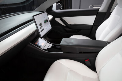 From the window next to the driver's seat, you can see the elegant black and white cockpit of a car, without a steering wheel, only with a touch display in the middle of the car.