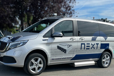 A branded Arnold NextG Mercedes EQV in silver stands in front of a tree under a blue sky.