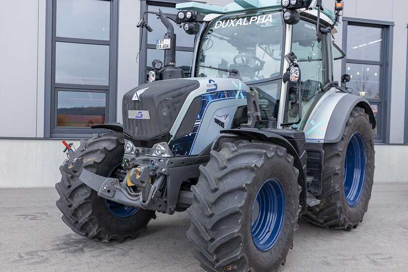 A silver-blue cyan tractor poses in front of a hall. 