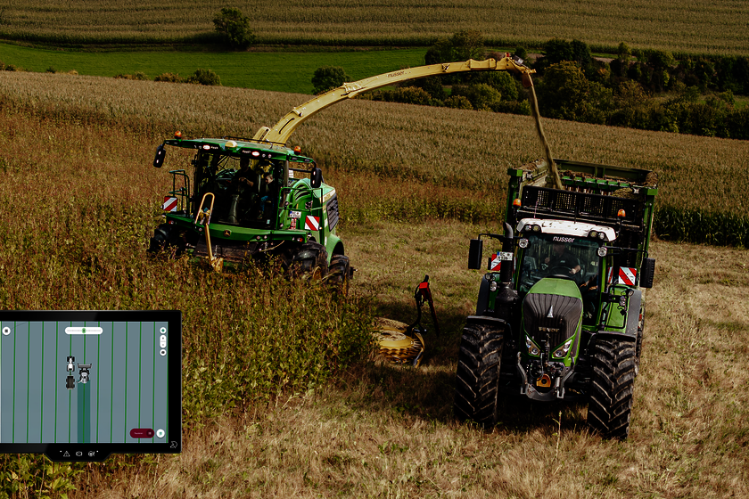 Two agricultural vehicles (a forage harvester and a tractor with a trailer) are driving through a silphium field and harvesting it. At the bottom left of the screen, you can see a touch display showing the two vehicles with track lines.