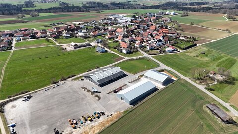 An aerial view of Aichelau Pfronstetten, coming from Ehestetten. The halls of the Next Mobility Campus can be seen at the bottom of the picture and Aichelau residential buildings in the background.