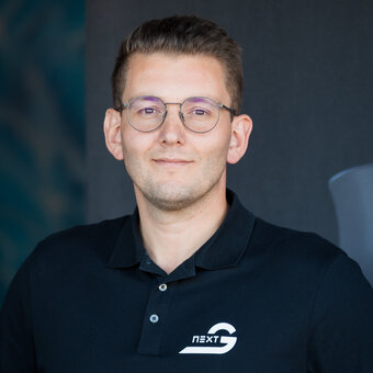 A middle-aged man smiling in front of a blue-black background, wearing thin glasses on his nose.