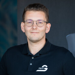 A middle-aged man smiling in front of a blue-black background, wearing thin glasses on his nose.