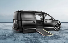 A lowered black VW Caddy, converted with NX NextMotion for self-driving vehicles, is parked in a large space with an open side access ramp - without a driver's seat.