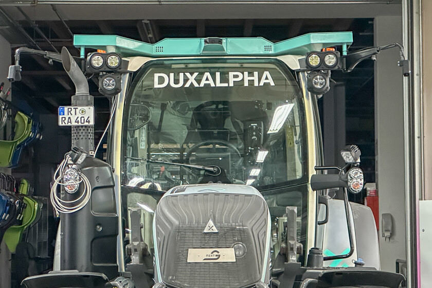 The front of a tractor that is cyan silver and features logos from Arnold NextG and DuxAlpha.
