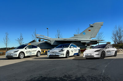 Three different Tesla vehicles are parked at an angle in front of a tornado against a blue sky. All are white with printing.