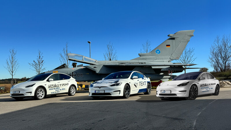 Three different Tesla vehicles are parked at an angle in front of a tornado against a blue sky. All are white with printing.
