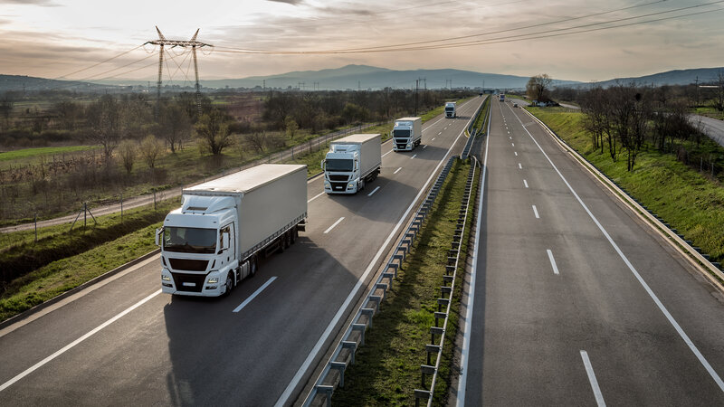 Several trucks drive at a perfect distance from each other as a platooning solution on the right lane of a highway.