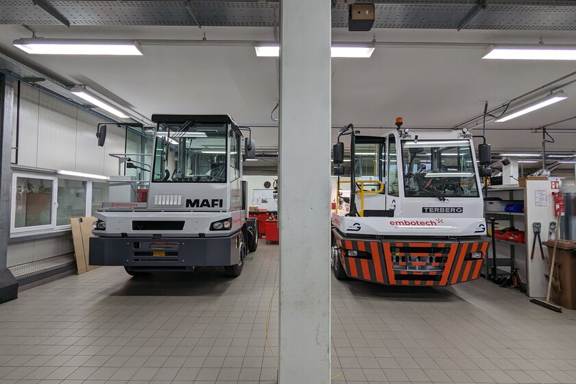Two terminal trucks are parked next to each other in Arnold NextG's workshop. The one on the left is gray and white and from the company MAFI Transport System GmbH and the one on the right is red and gray and white from the company Terberg.