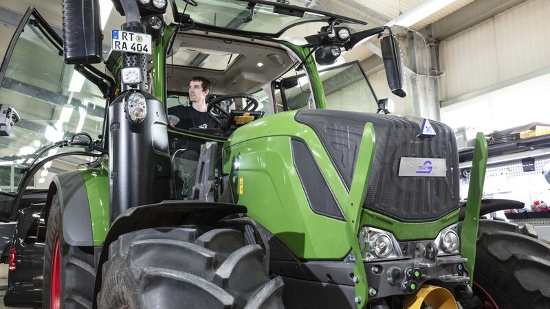 A light green tractor, retrofitted with NX NextMotion, is tested by a technician in the workshop while sitting in the cab.