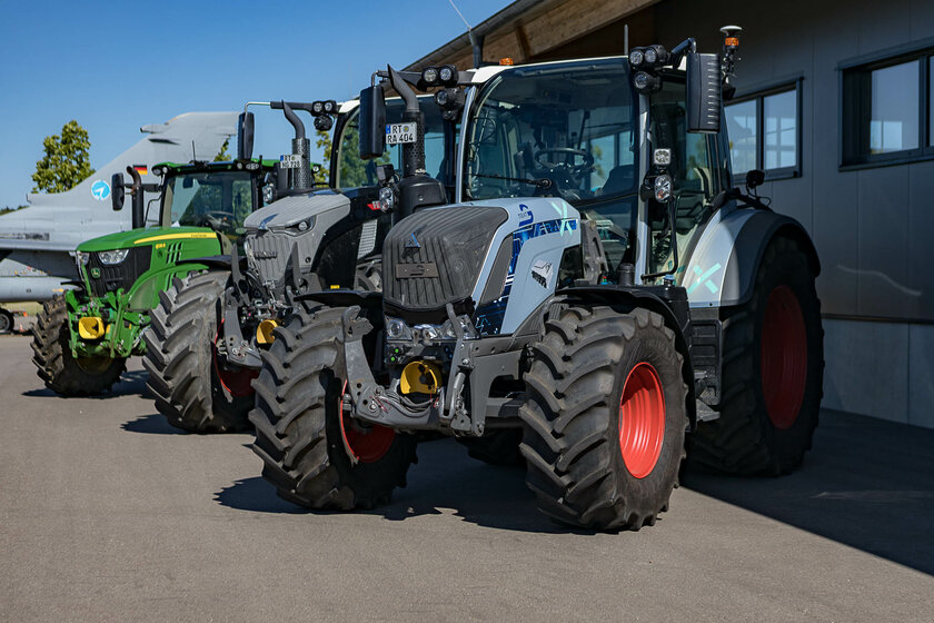 Three different colored tractors from different manufacturers stand next to each other in bright sunlight. 