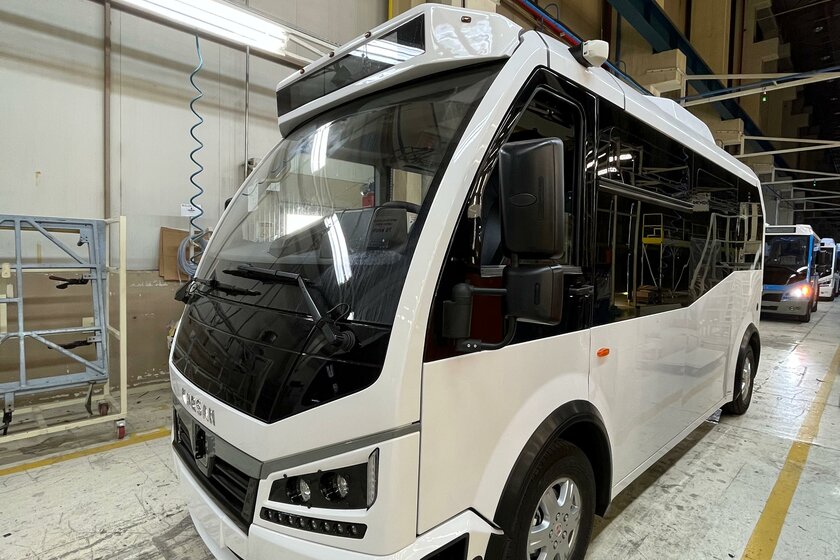 A white bus is parked in a warehouse. Other vehicles are parked at a distance behind it.