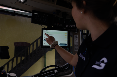 A woman is sitting in a booth and pressing a touch display with one finger.