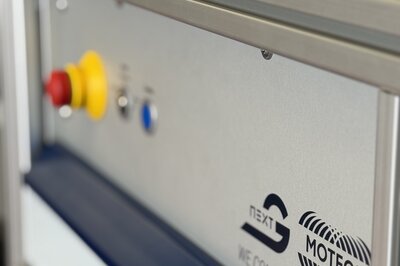 A metal plate with a yellow and red button in the background and two logos on the front. One is Arnold NextG and the other Moteon.